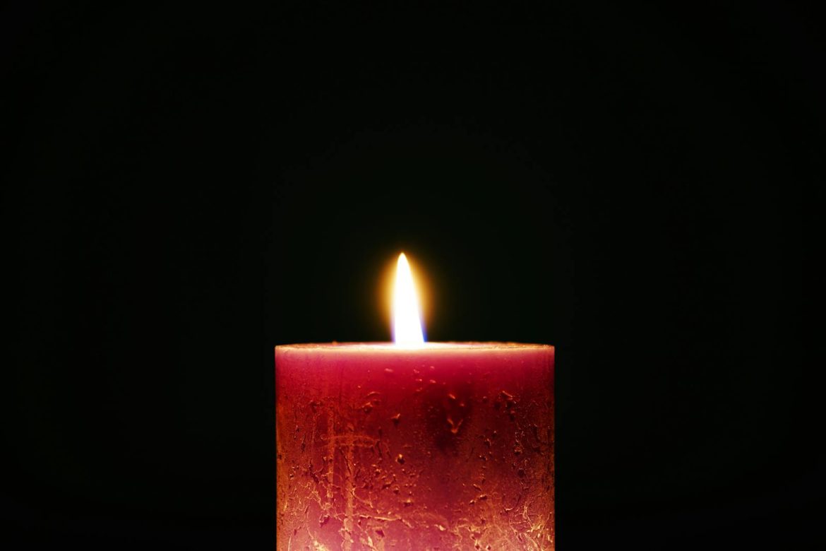 A solitary red candle with a bright flame against a dark background, creating a serene atmosphere.