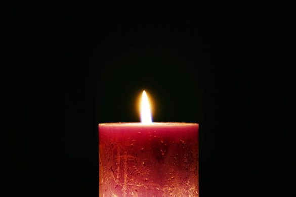 A solitary red candle with a bright flame against a dark background, creating a serene atmosphere.