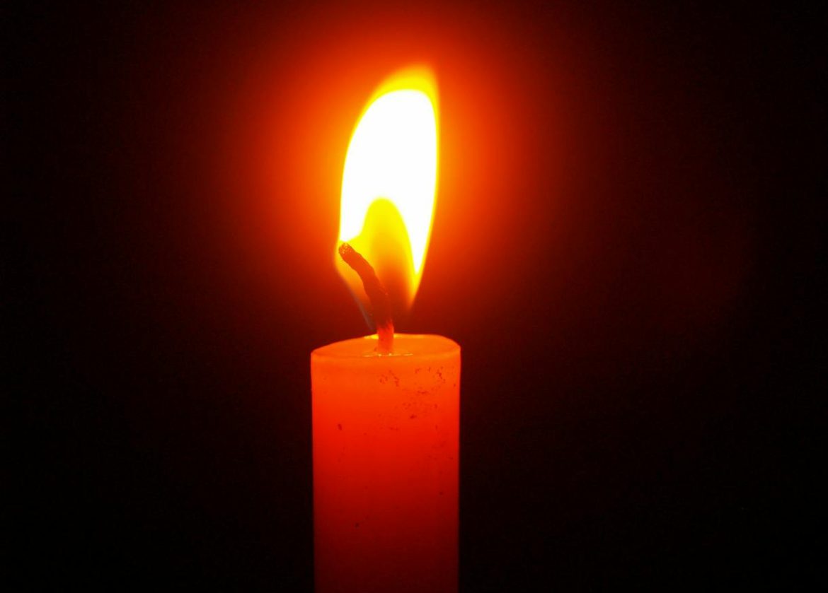 A single candle flame illuminating the darkness, symbolizing warmth and hope.