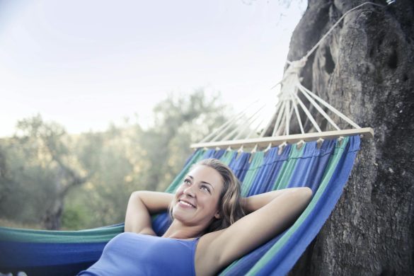 A young woman smiling and relaxing in a hammock outdoors during summer.