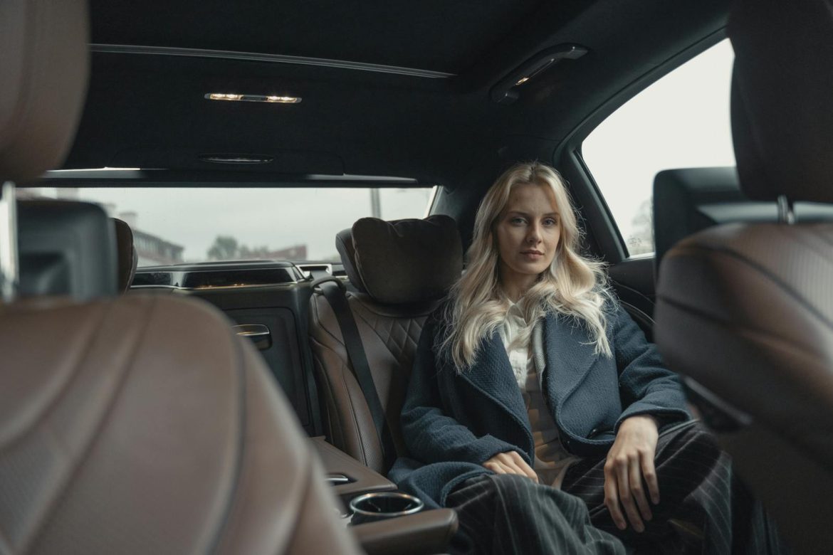 Elegant woman in a blue coat sitting in the back seat of a luxury car.