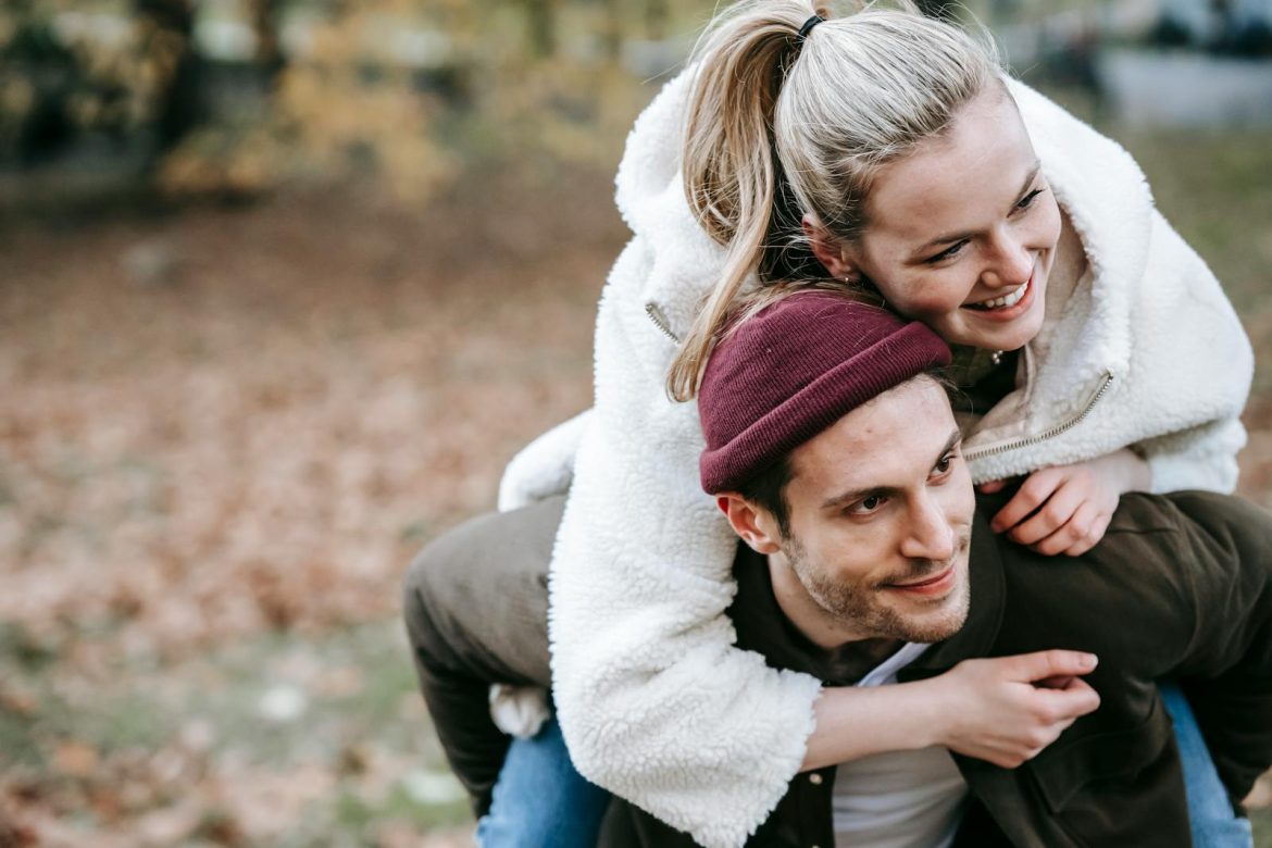 Cheerful couple sharing a joyful moment with a piggyback ride in a scenic autumn park setting.