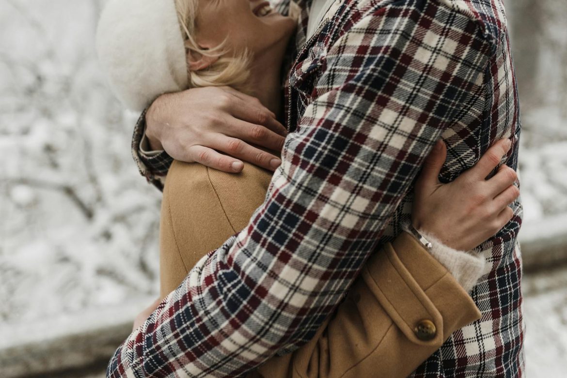 A couple embracing outdoors during winter wearing warm clothing, exuding affection.