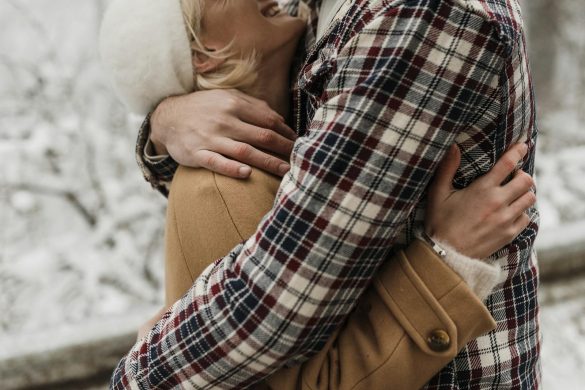 A couple embracing outdoors during winter wearing warm clothing, exuding affection.