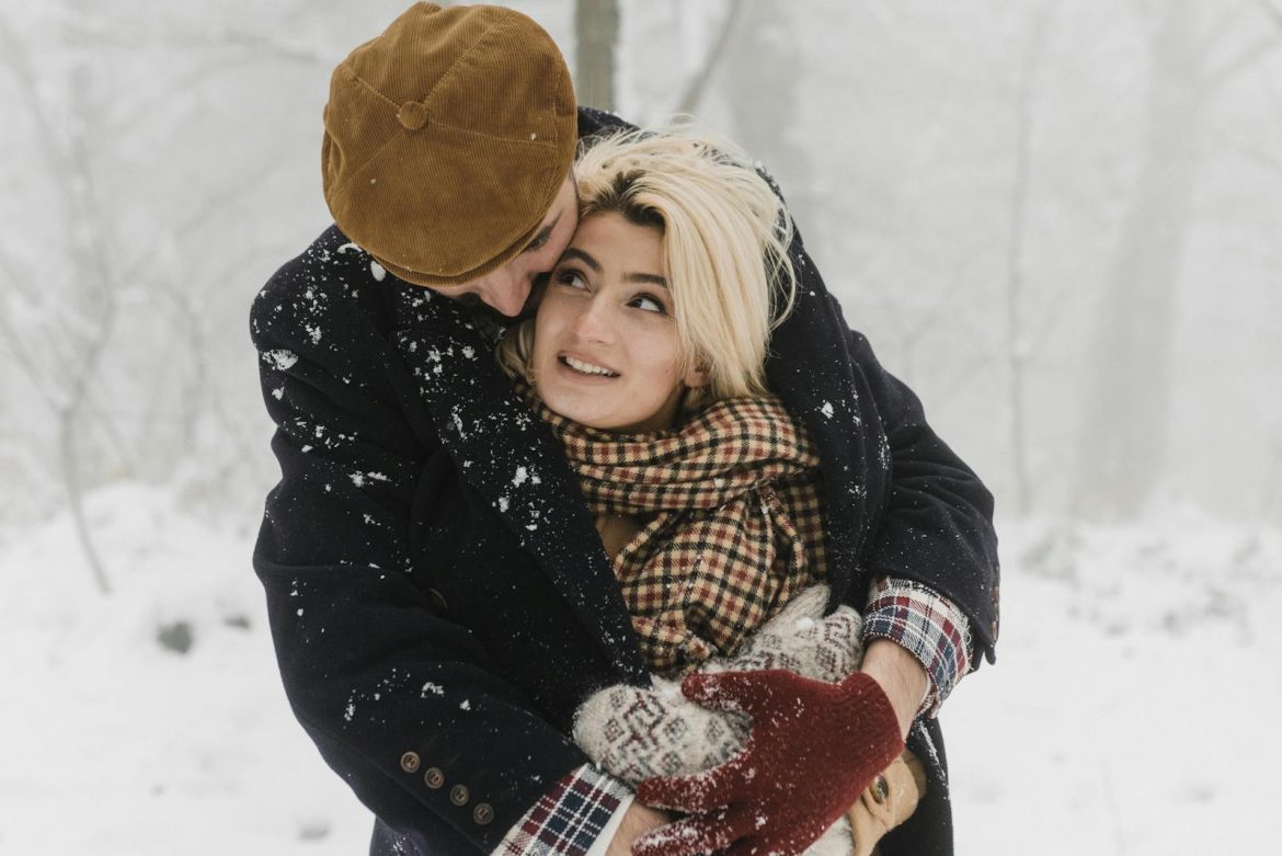 A loving couple embraces in a snowy forest, capturing a romantic winter moment.