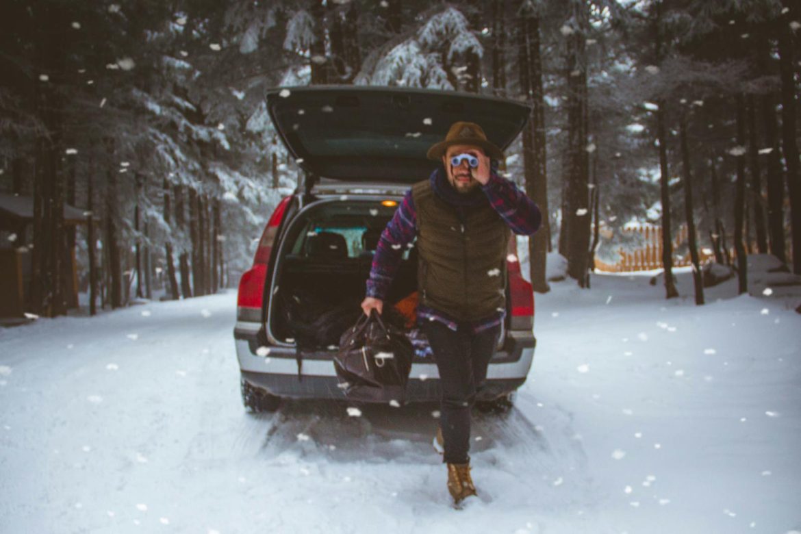 Man preparing for winter journey with open car trunk on snowy forest road in Bursa, Turkey.