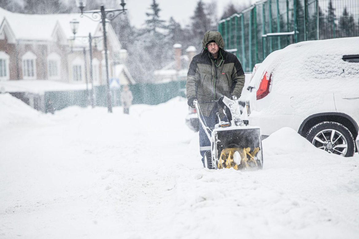 A man using a snow blower to clear snow from a snowy street during winter.