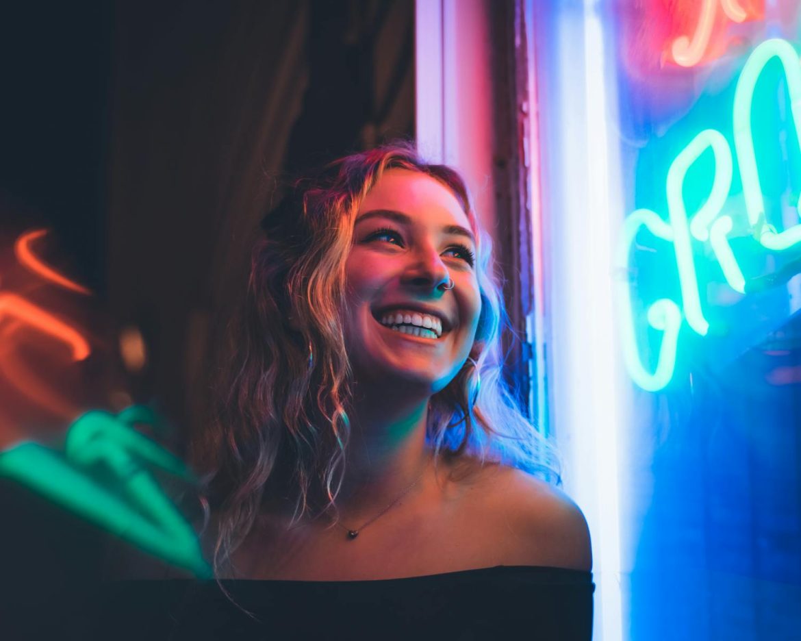 Portrait of a smiling woman with neon lights illuminating her face, capturing a vibrant nighttime atmosphere.