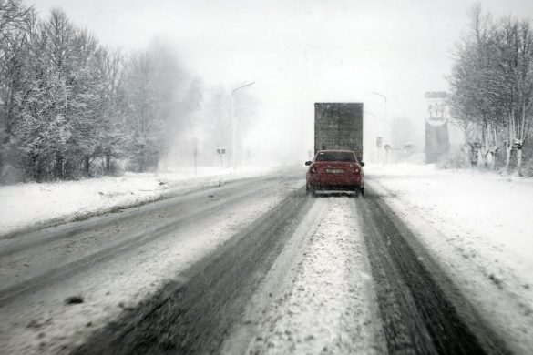 Cars navigate a snowy highway during a blizzard, showcasing tough winter driving conditions.