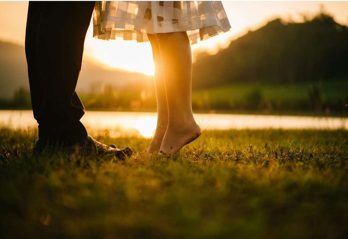 A romantic moment captured at sunset by a tranquil lakeside, showcasing togetherness.