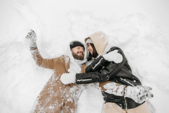 A couple lying in snow, enjoying a romantic winter moment together outdoors.