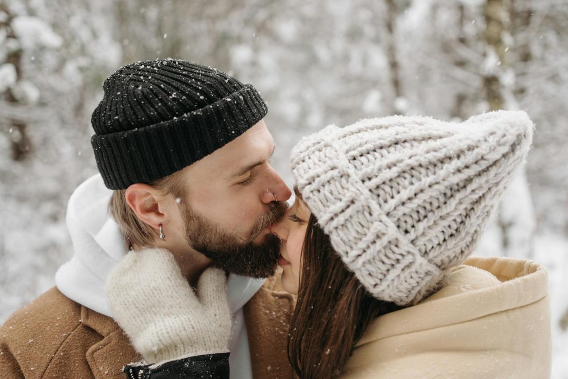 A couple embraces warmly, sharing a kiss amidst a serene snowy backdrop, capturing winter romance.