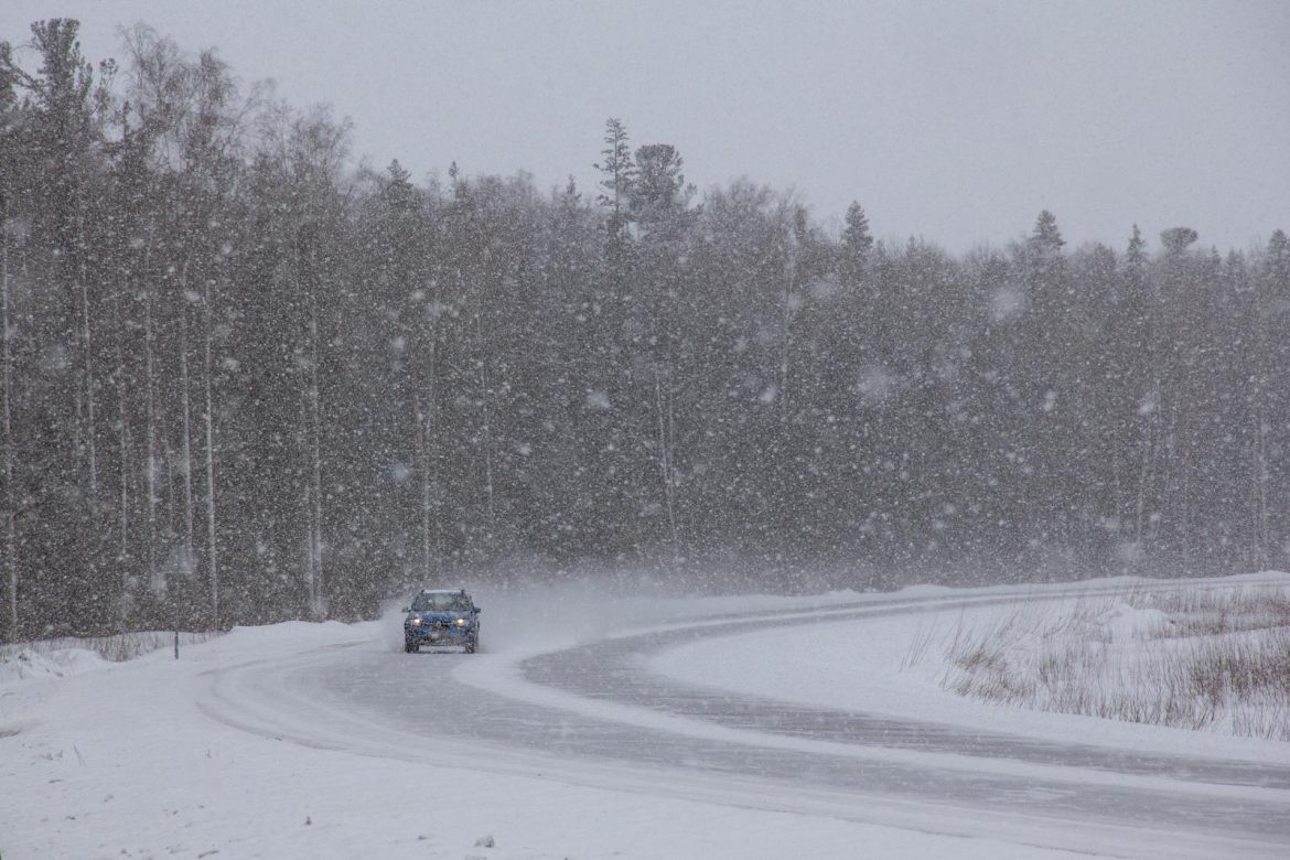 A car navigates a snowy forest road during a winter snowstorm, capturing the harsh weather conditions.