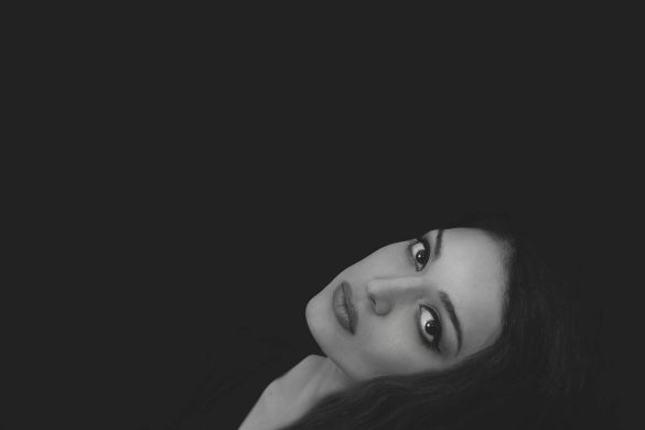 A striking black and white portrait of a woman with a serious expression on a dark background.