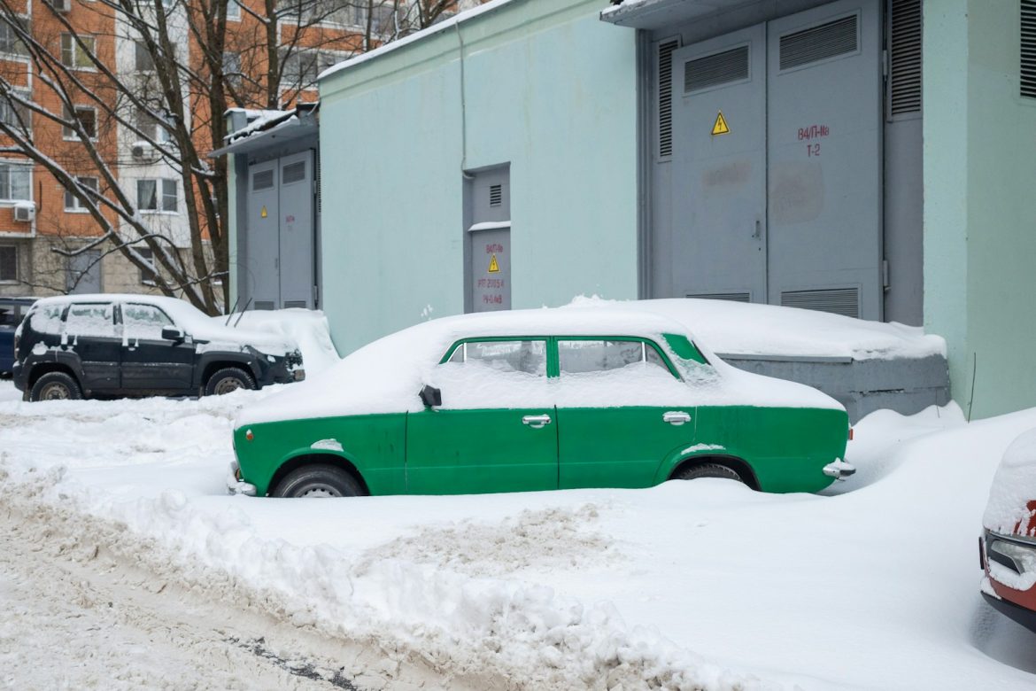a green car is parked on a snowy street