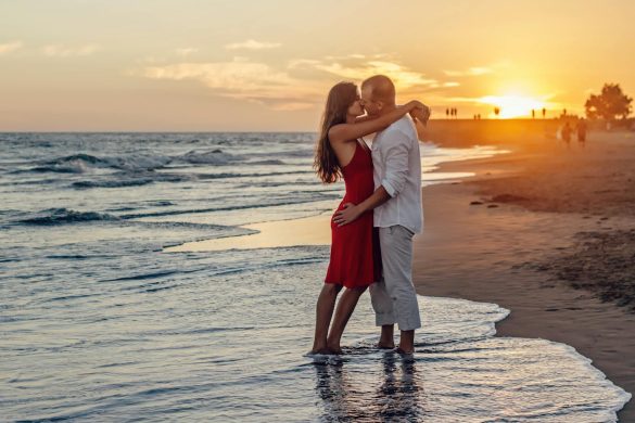 A couple in love embraces at the seaside during a vibrant sunset.