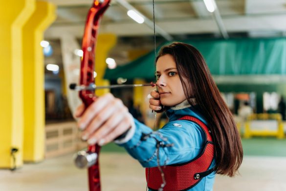 Young woman practicing archery indoors, showcasing skill and determination.