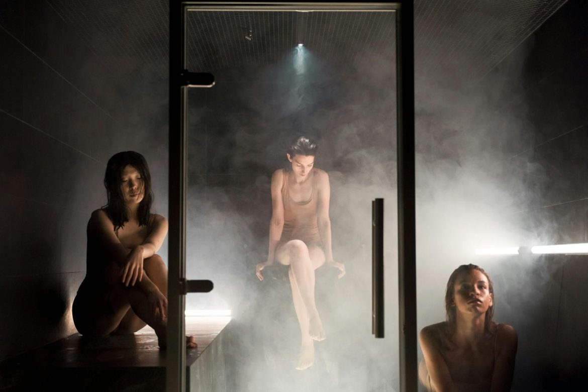 Three women enjoying the calming atmosphere of a steam-filled sauna for relaxation and wellness.