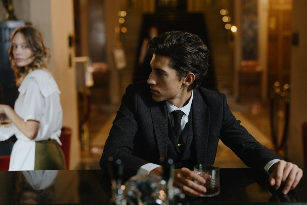 Stylish couple at a bar, man in suit with whiskey, ambient mood.