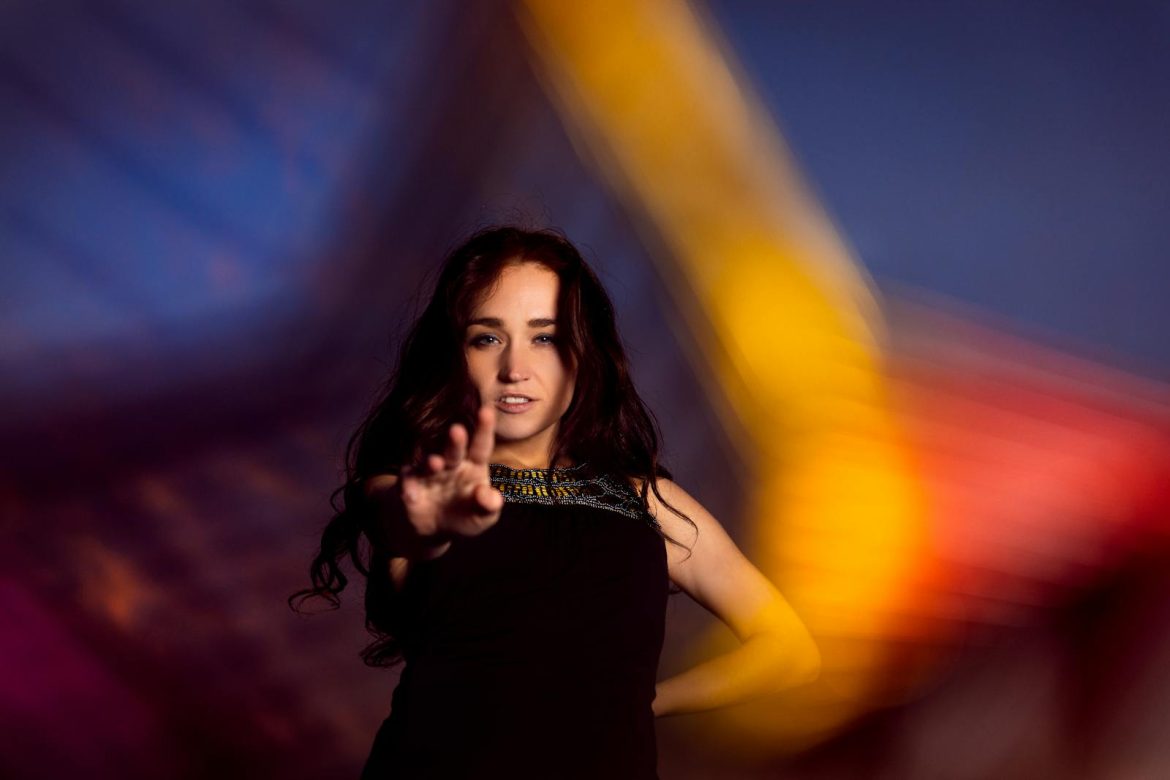 A woman reaches out in a colorful, blurred background setting, creating an artistic effect.