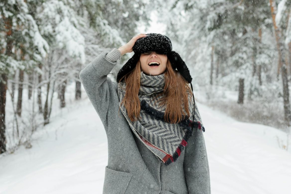 Happy woman in winter coat and scarf laughing in snow-covered forest in Russia.