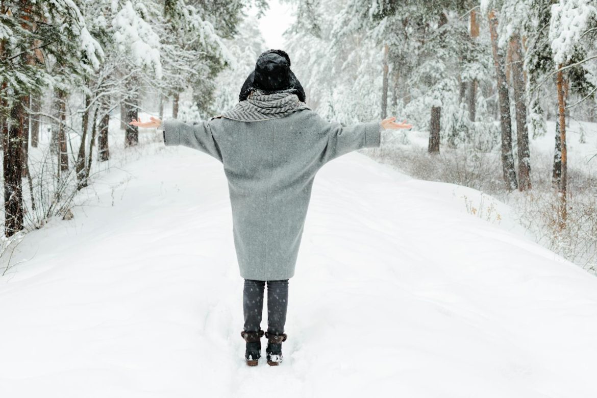 Back view of a woman embracing a snowy winter scene in a Russian forest.