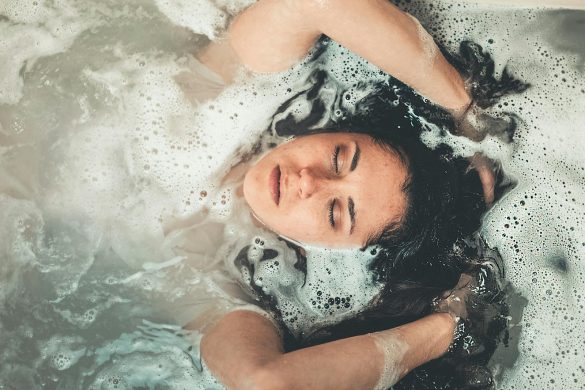 Calm and serene young woman enjoying a bubble bath with her eyes closed.