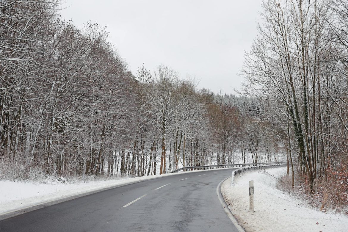 A peaceful winter scene of a country road winding through a snow-covered forest.