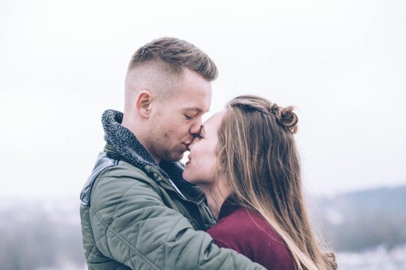 A romantic couple kisses outdoors on a chilly day, conveying warmth and affection.