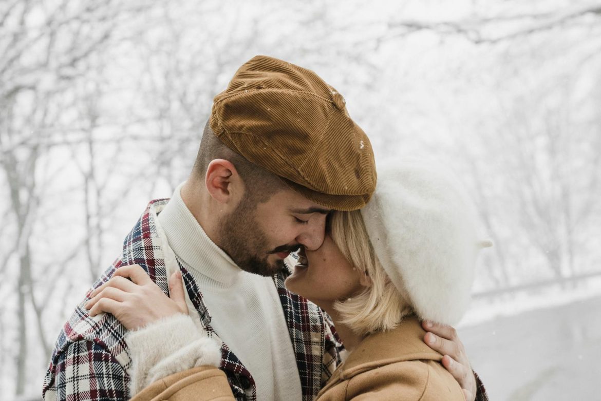 A joyful couple shares an intimate moment surrounded by a snowy landscape, showcasing their love.