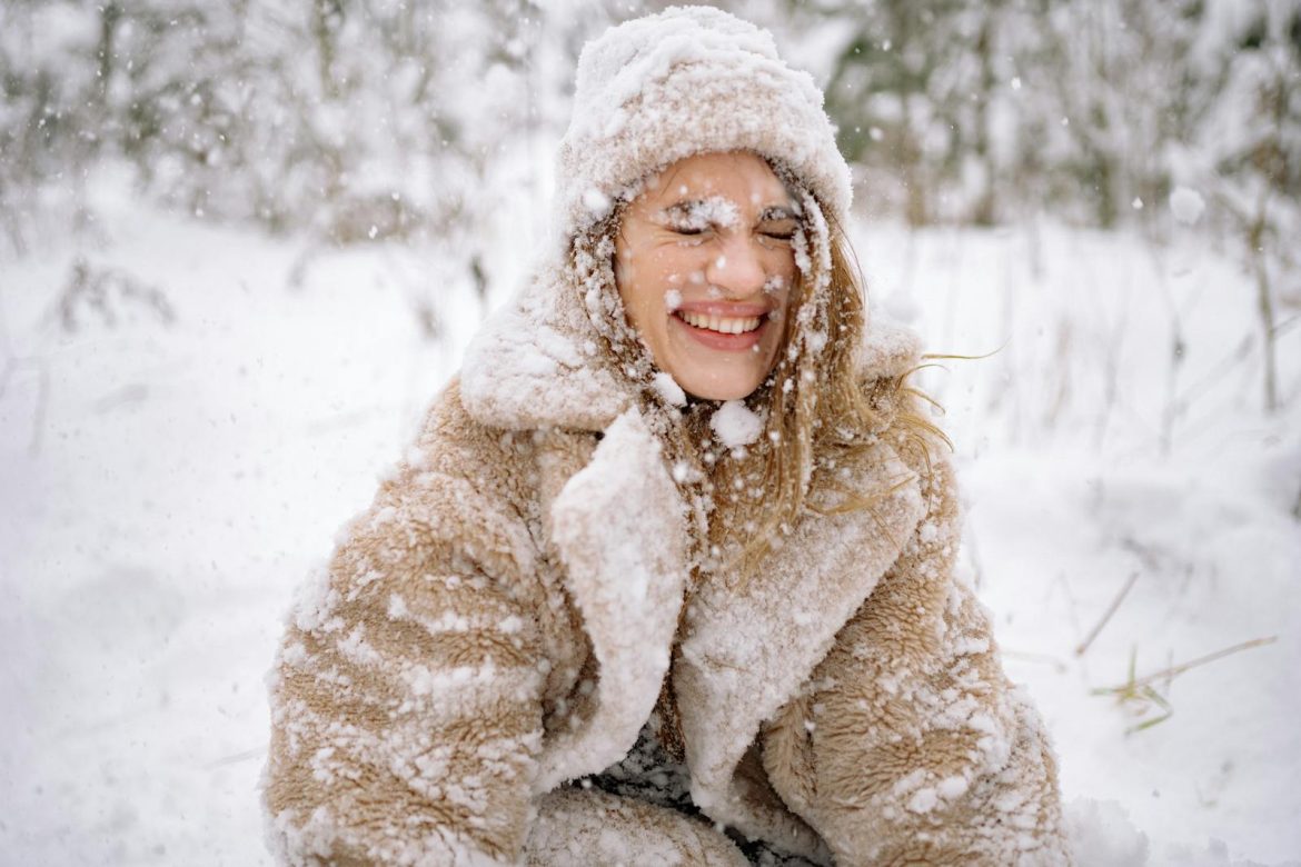Smiling woman enjoying a snowy day outdoors, embracing the winter season in warm clothing.