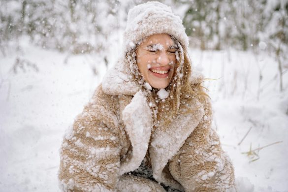 Smiling woman enjoying a snowy day outdoors, embracing the winter season in warm clothing.