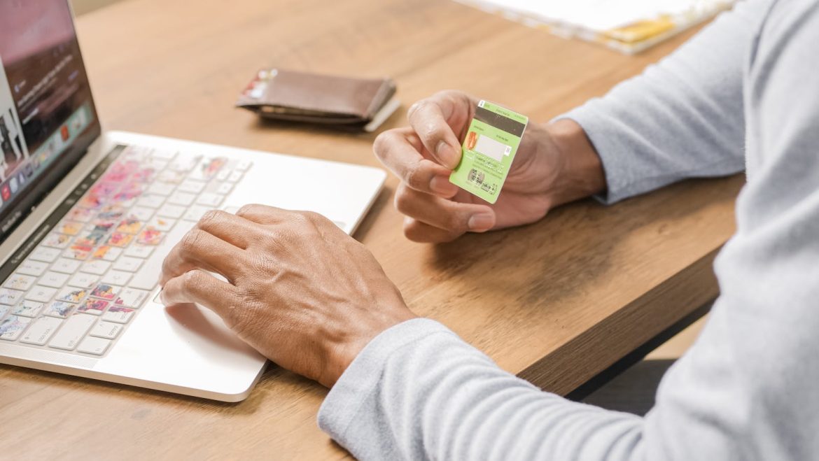 Person holds a credit card while browsing on a laptop, symbolizing convenient online shopping.