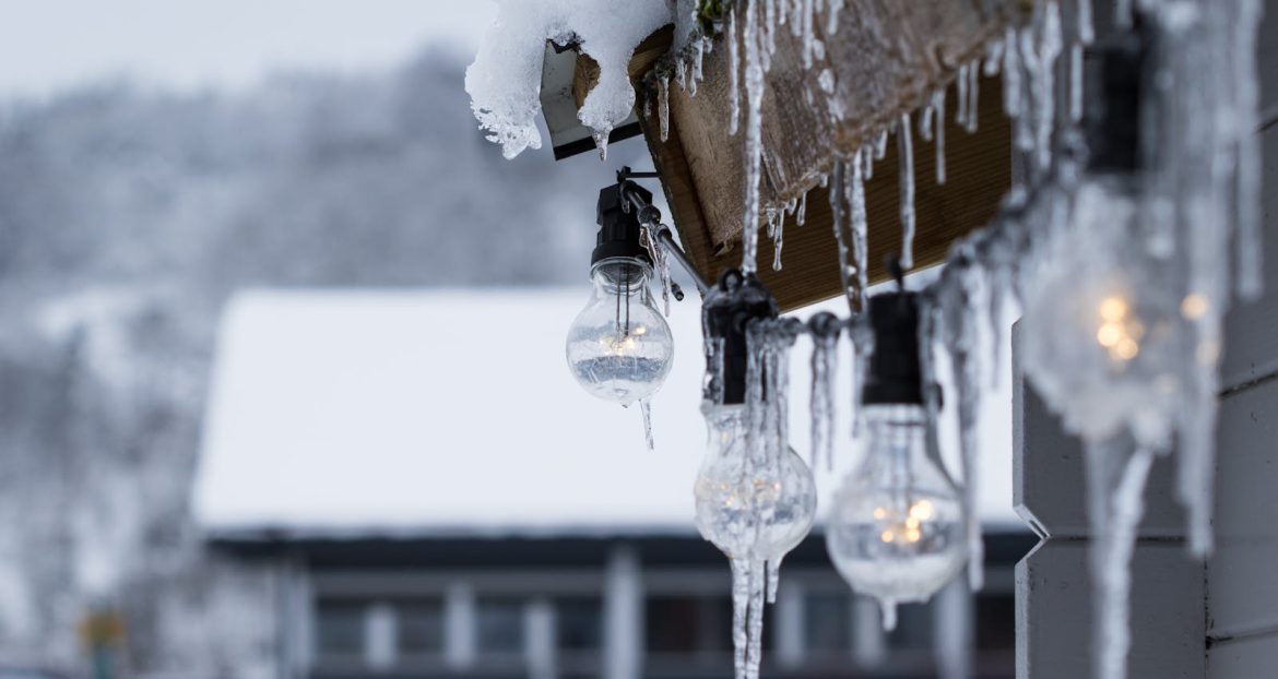 Close-up of hanging lightbulbs covered in icicles against a snowy winter backdrop.