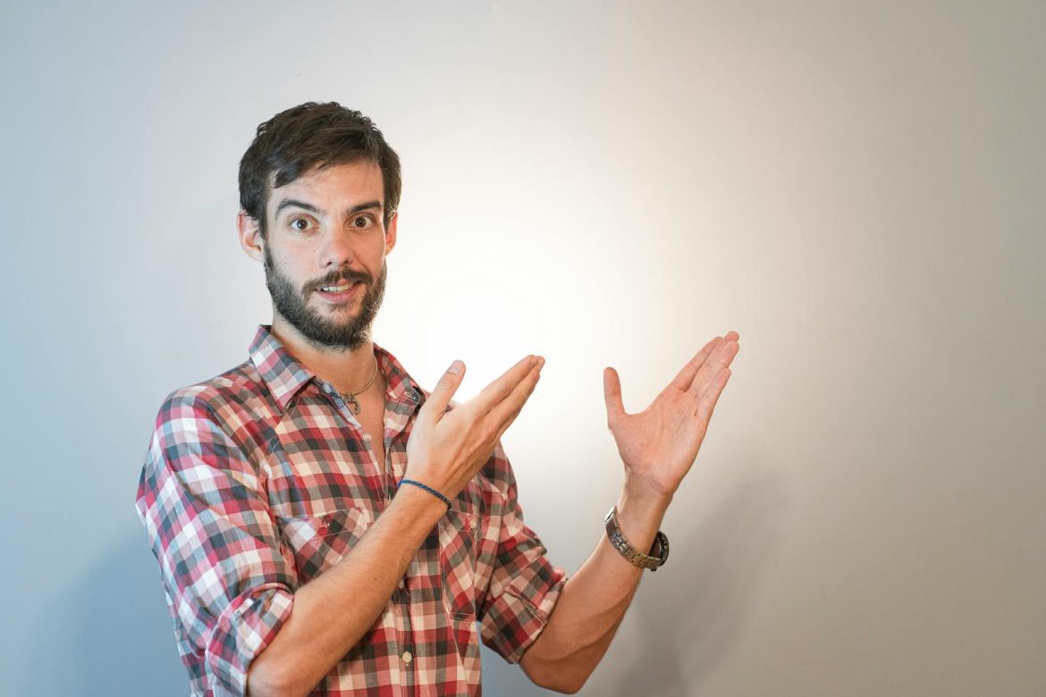 Engaging portrait of a bearded man with raised hands, pointing enthusiastically against a white background.