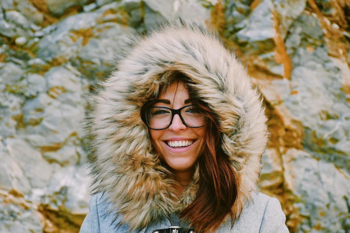 Portrait of a happy woman in a fur-lined hooded coat against a rocky background outdoors.