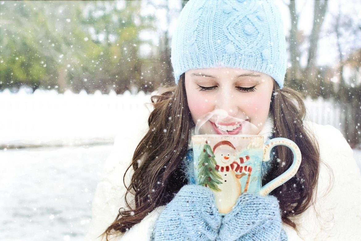 A woman savoring hot chocolate amidst falling snowflakes, capturing cozy winter vibes.