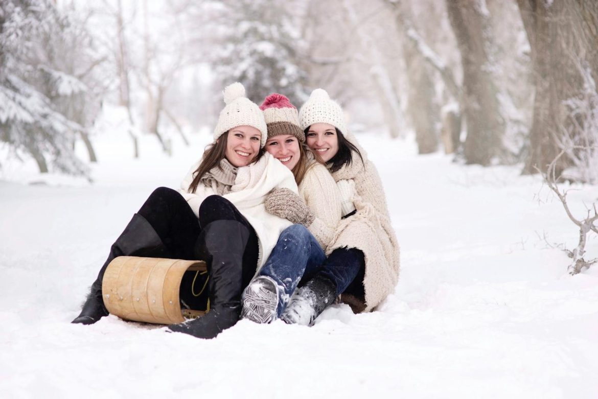 Three women laughing and sledding in a snowy forest, exuding joy and winter fun.