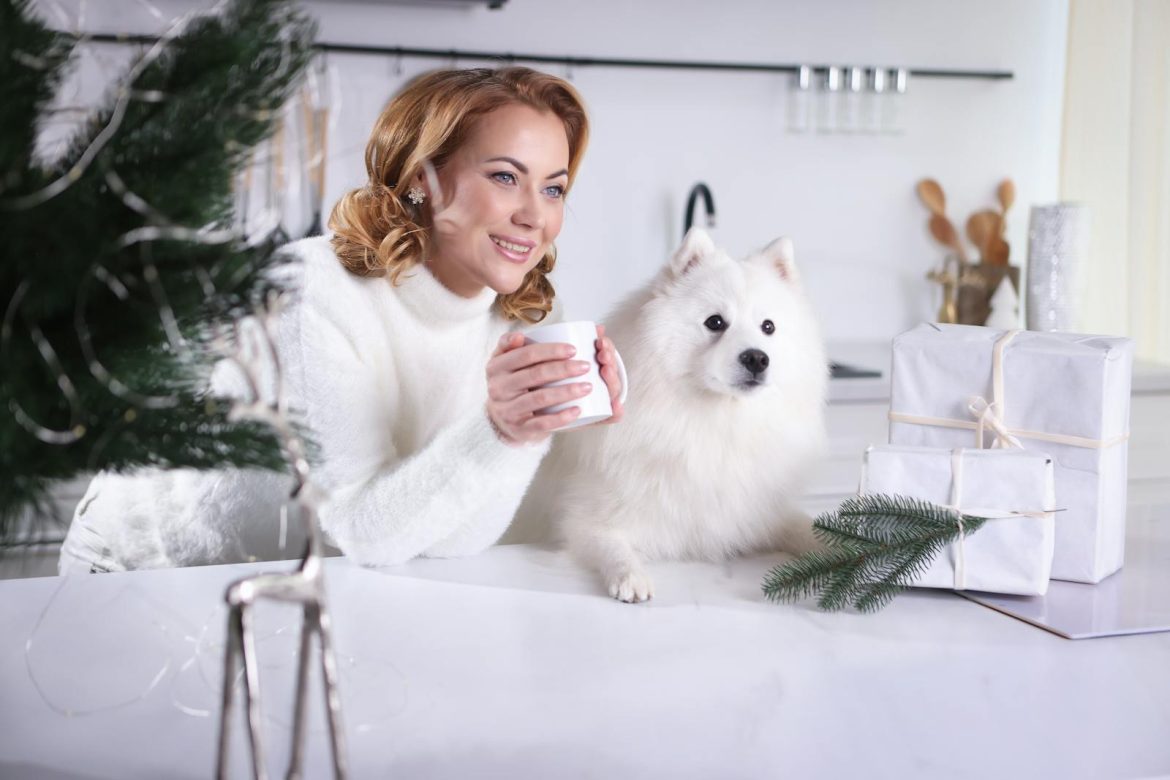 Woman holding a mug with gifts and fluffy dog. Cozy winter scene indoors.
