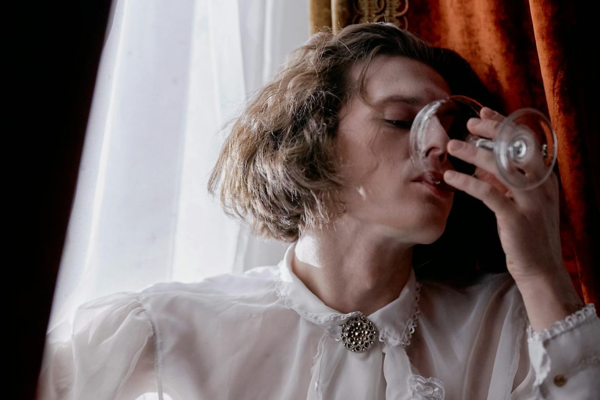 Close-up portrait of an adult enjoying wine in vintage attire indoors.