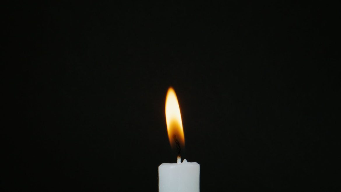 A serene close-up of a candle flame gently shining against a dark background, evoking calm and tranquility.