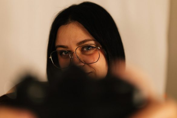 Young woman with glasses holding camera in foreground