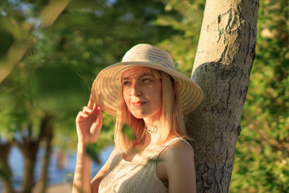 A woman in a hat enjoying a sunny day outdoors against a tree.