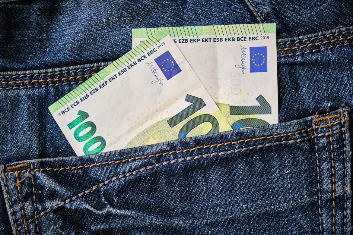 Close-up of Euro currency notes peeking from a blue denim jeans pocket.