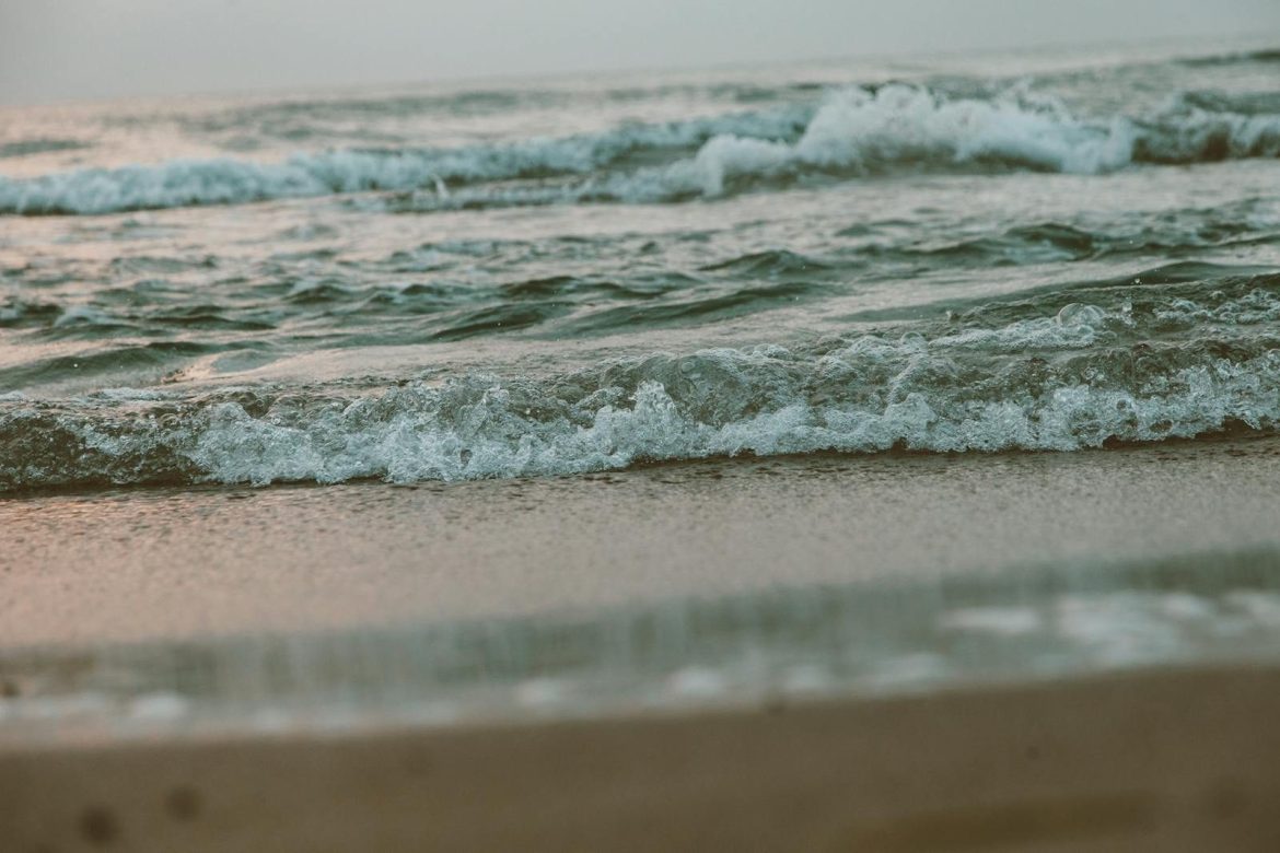 Tranquil scene of gentle ocean waves rolling onto a sandy beach shore at sunset.