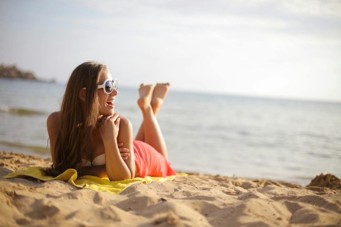 Enjoy carefree summer vibes with a young woman sunbathing on a sandy beach.