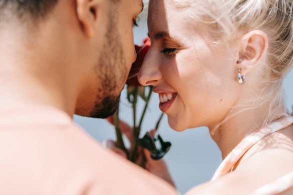 Close-up of a couple smiling, sharing a romantic moment with a rose outdoors.