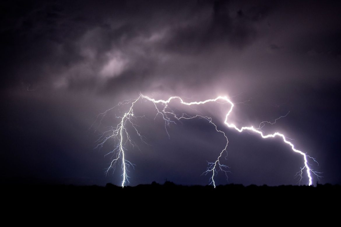 Vivid lightning bolts illuminate the dark night sky over an open field creating a striking natural display.