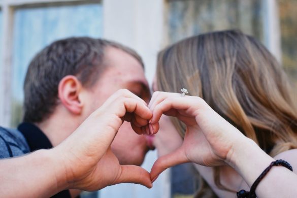 Close-up of a couple kissing behind a heart-shaped hand gesture, symbolizing love and connection.