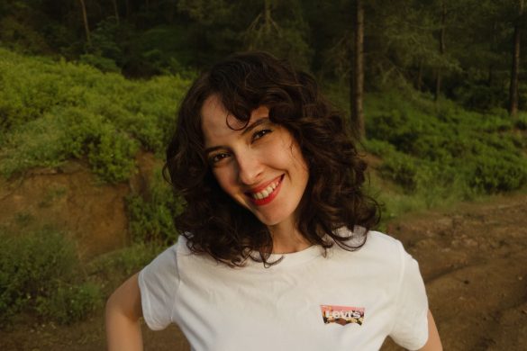 A cheerful woman with curly hair smiling outdoors in a green forest setting.